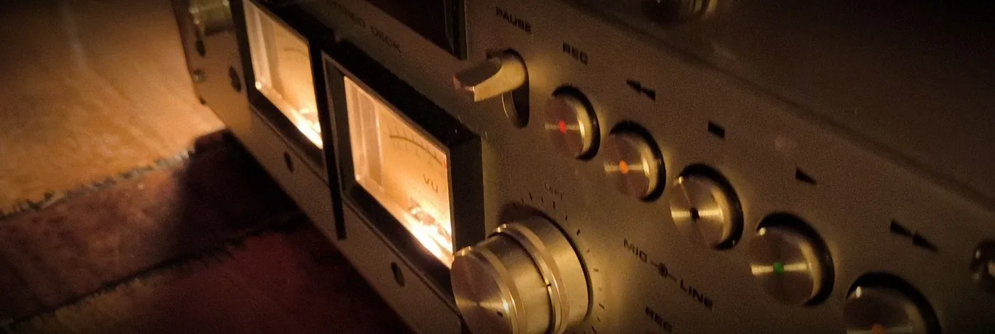Die beiden beleuchteten Anzeigen der Bandmaschine, daneben die Tasten und Regler im warmen Licht.