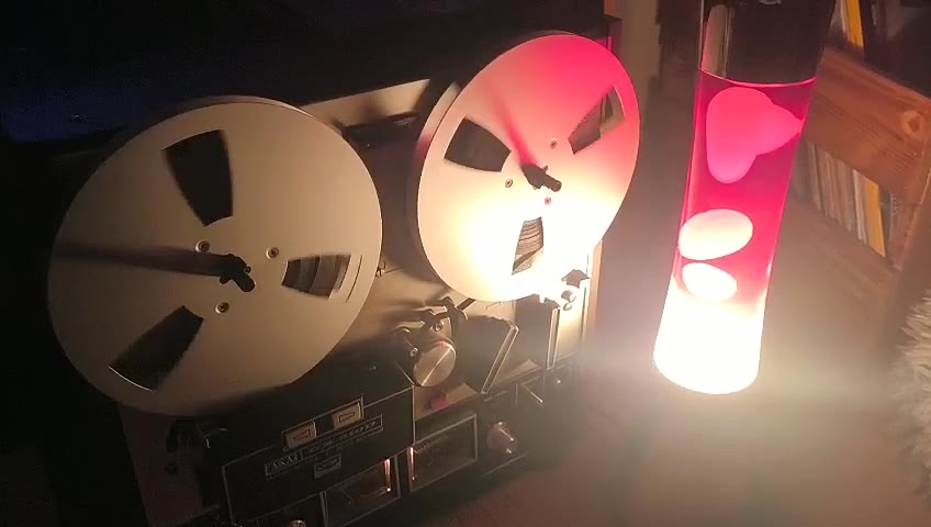 Die Bandmaschine im abgedunkelten Raum, daneben leuchtet eine Lavalampe